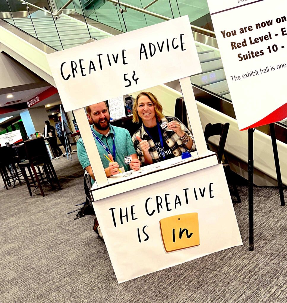 Two teachers are smiling behind a sign that declares, "The Creative Is In."